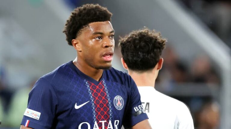 Jeune footballeur en maillot du Paris Saint-Germain, regard pensif sur un terrain d'entraînement.