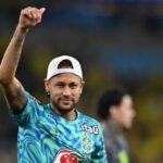Neymar souriant sous le maillot du Brésil, sur un terrain de football.