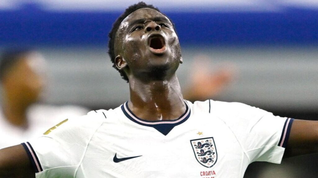 Bukayo Saka en maillot de l'Angleterre, avec un fond flou évoquant le stade d'un Mondial, une aura de mystère.