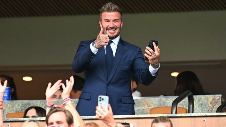 David Beckham souriant dans une loge VIP lors d'un match de la Coupe du monde 2026, entoure de partenaires publicitaires