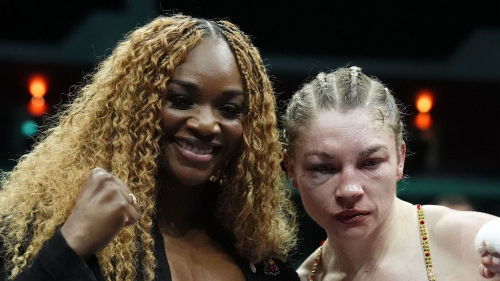 Combat de boxe féminine avec gants rouges et bleus sous les projecteurs d'un ring lumineux.