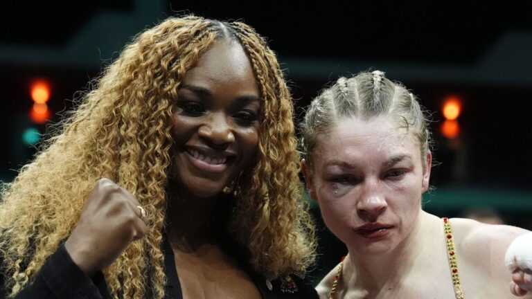 Combat de boxe féminine avec gants rouges et bleus sous les projecteurs d'un ring lumineux.